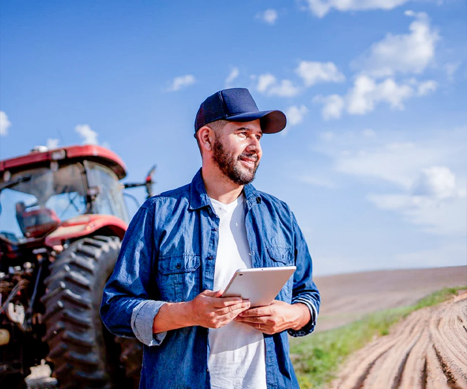 Homem no agronegócio usando tablet em frente a um trator, simbolizando automação IFRS 16 no agronegócio