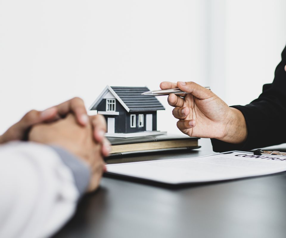 Reunião entre cliente e consultor discutindo financiamento imobiliário com modelo de Plano Empresário, com miniatura de casa sobre a mesa.