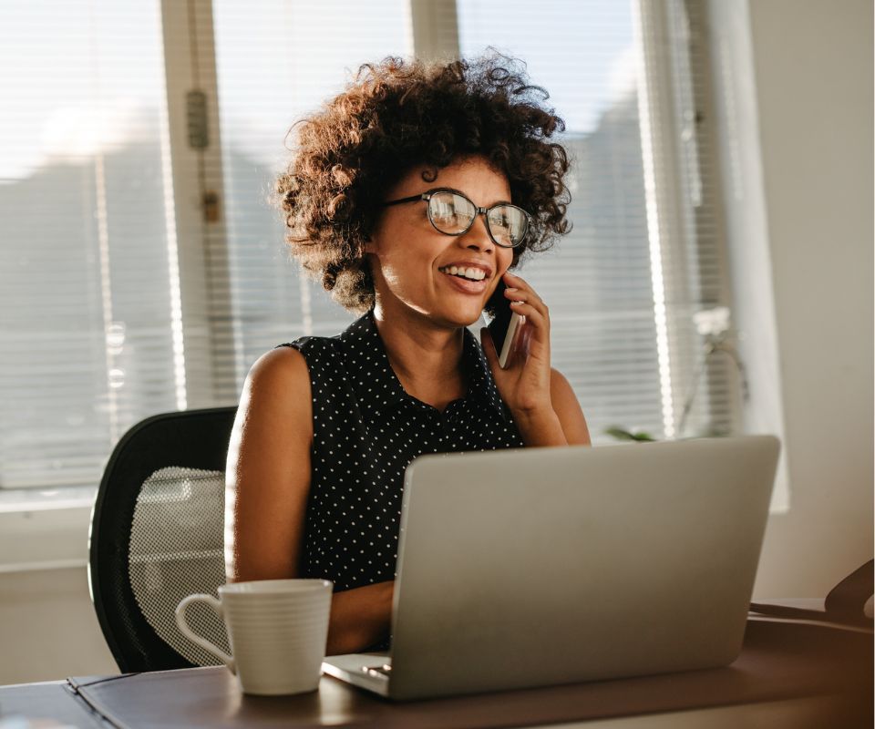 Mulher sorrindo ao telefone Profissional sorrindo ao telefone enquanto trabalha no notebook em um escritório, ilustrando processos de come-cotas e automação financeira.